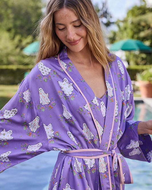 Person wearing a purple robe with white ghost and floral prints beside a swimming pool.