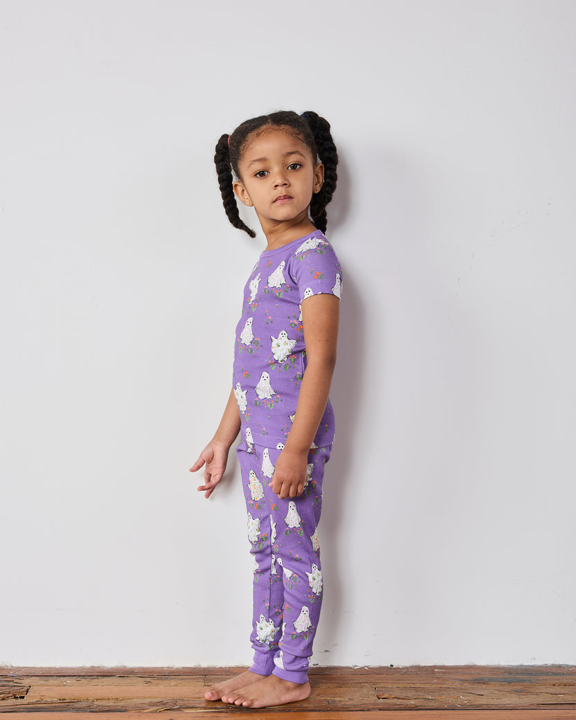 Child wearing a purple short-sleeve pajama top and pants with a ghost-and-floral print