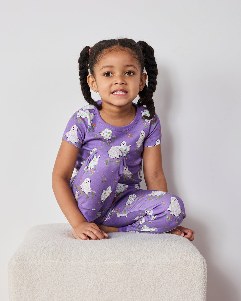 Child seated cross-legged wearing a purple short-sleeve ghost-print pajama set