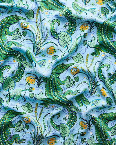 Blue Lagoon fabric swatch with repeated green alligators, leaves, vines, and small orange flowers.