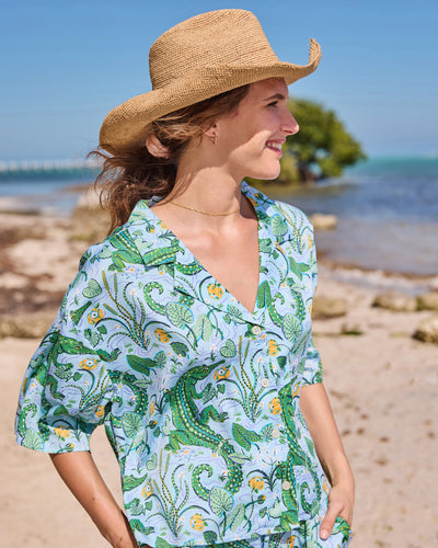 Waist-up view of the button-front gator-print pajama top worn with matching pants on a beach
