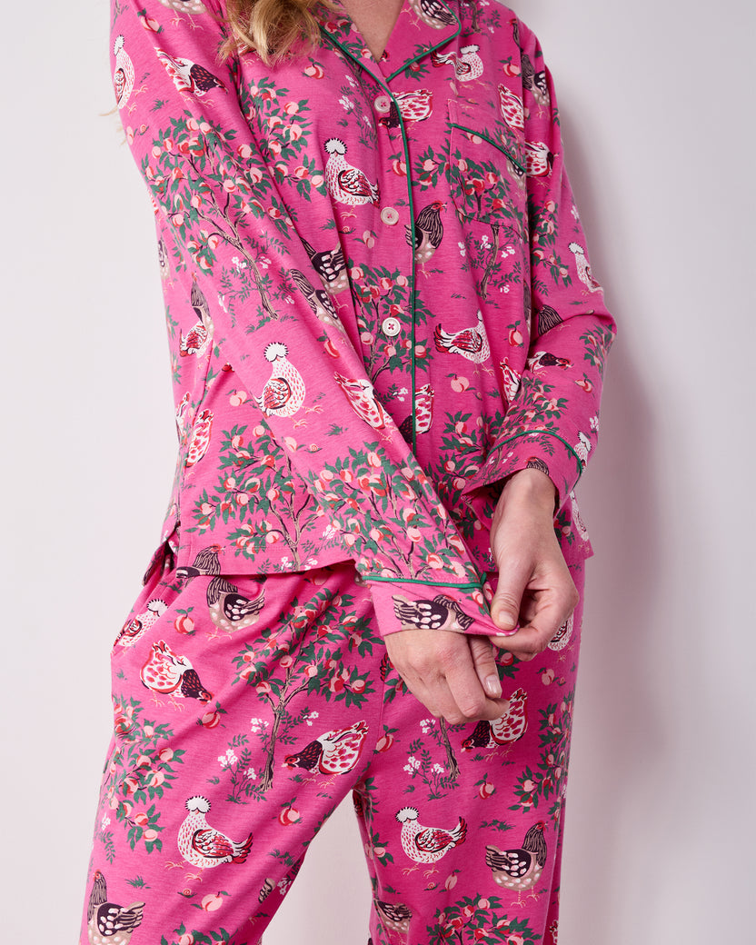 Close front view of the Rose Pop Hen House pajama top and matching pants, showing the button front, green piping, chest pocket, and chicken-and-floral print.