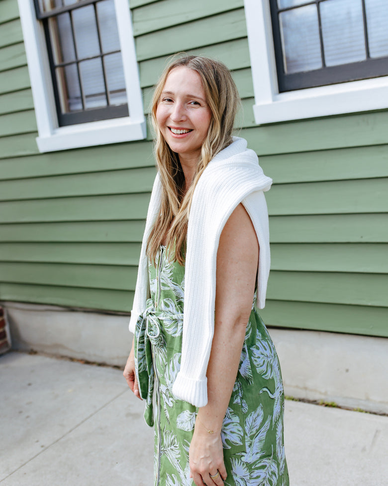 Side view of the Heron Landing Alma Dress with the waist belt tied in a bow and a white sweater draped over the shoulders