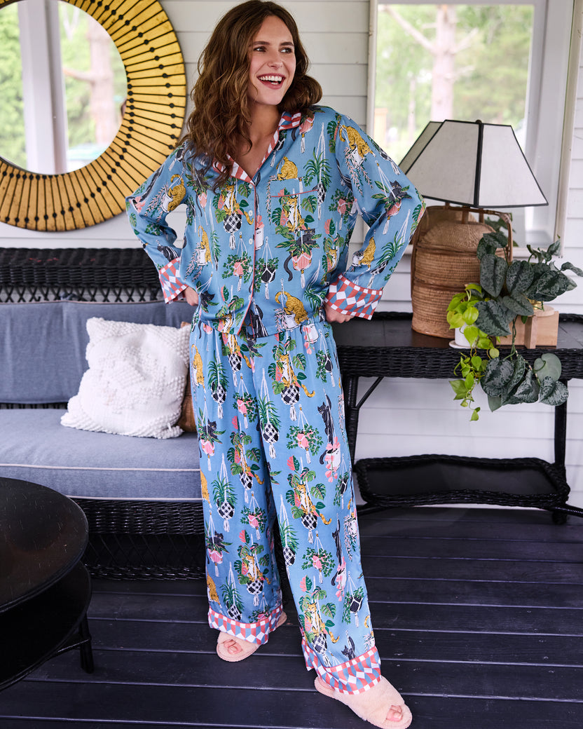 Model standing indoors wearing the slate blue Macrame Mischief long pajama set with a cat, plant, and pineapple print.