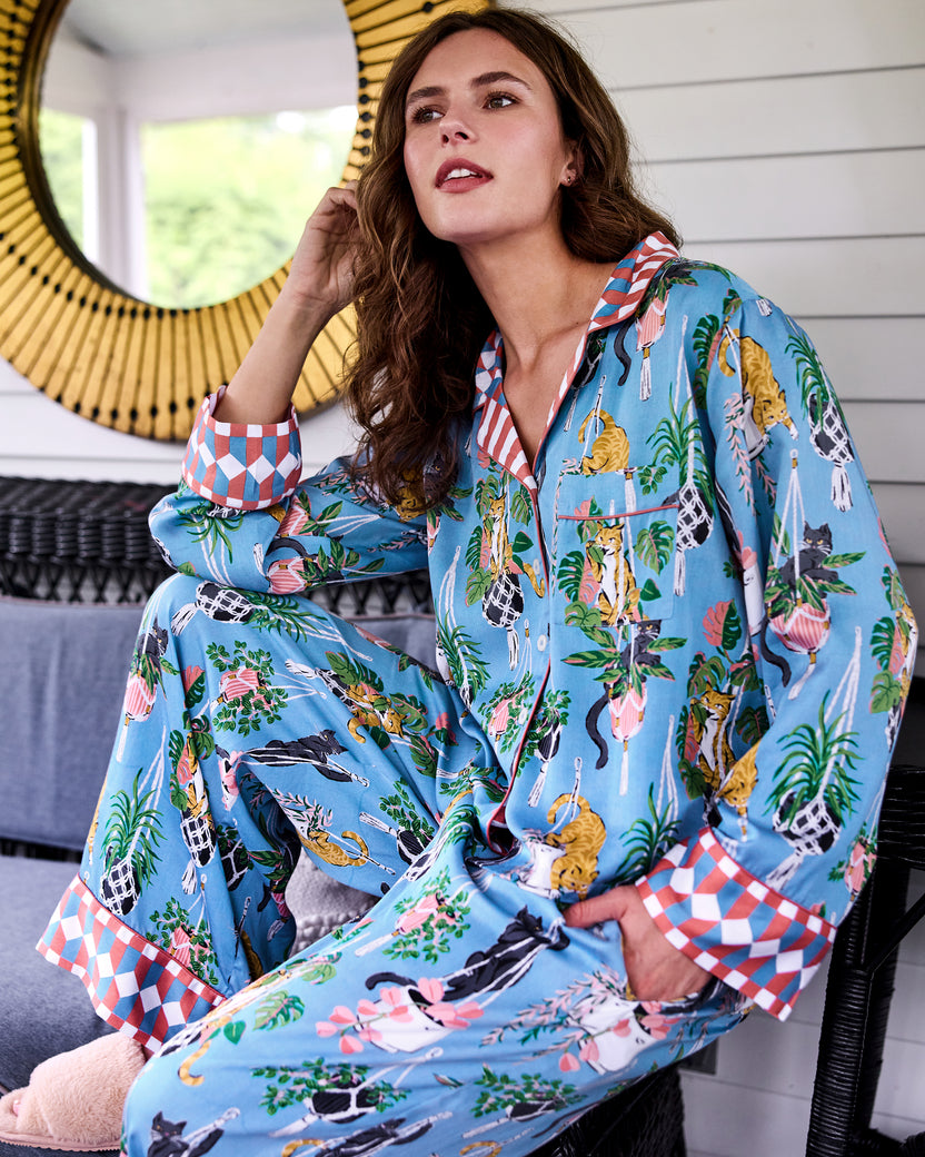 Person seated indoors wearing a blue pajama set with cat, houseplant, and geometric cuff prints.