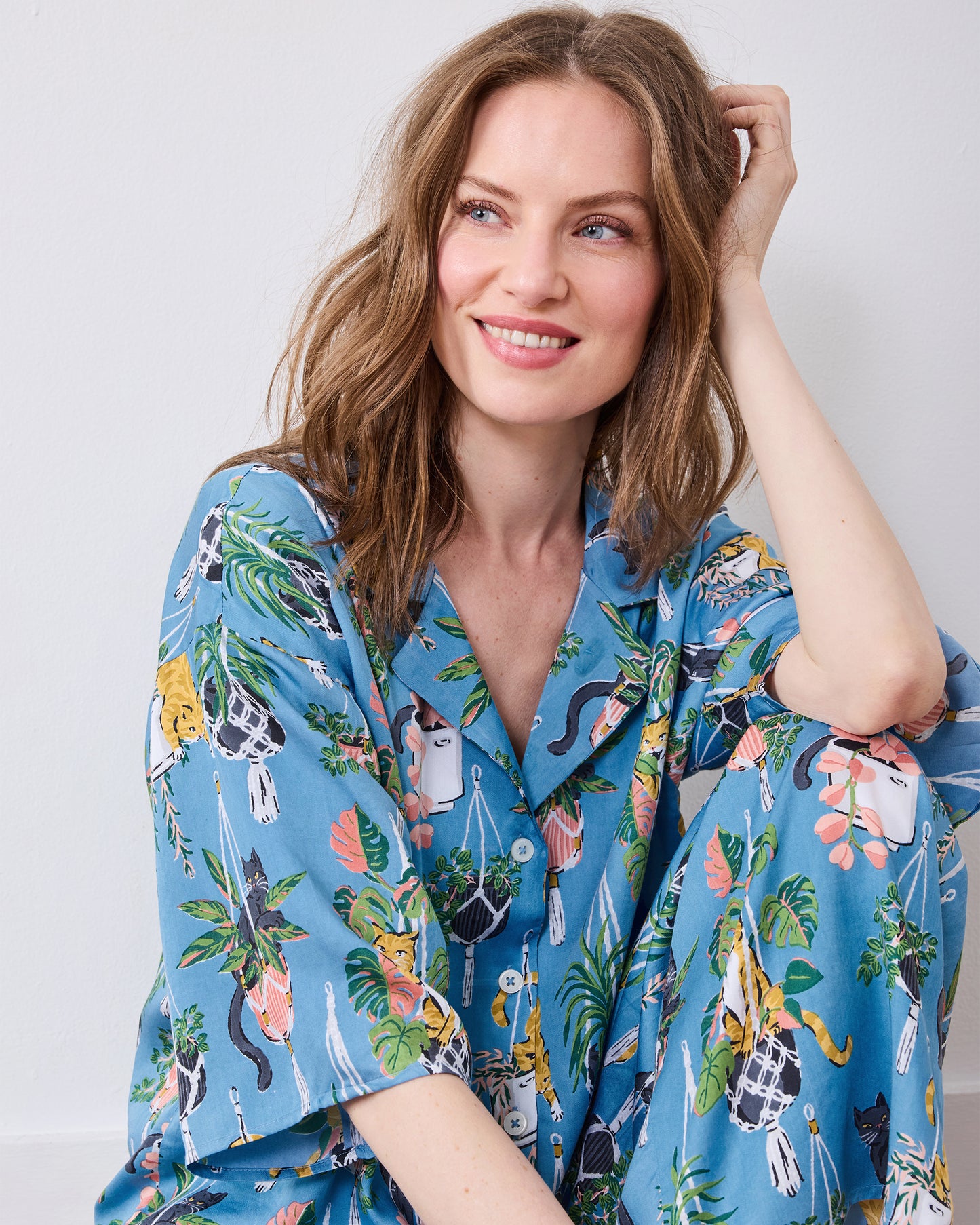 Seated model wearing the slate blue pajama set with cat and houseplant print