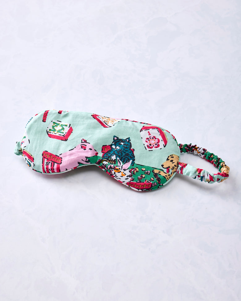 Pale jade eye mask with an adjustable printed strap and Mah Jongg-themed animal and game-table print.