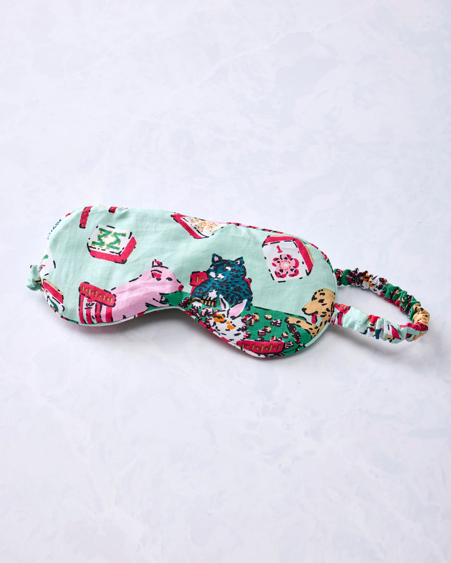 Pale jade eye mask with an adjustable printed strap and Mah Jongg-themed animal and game-table print.