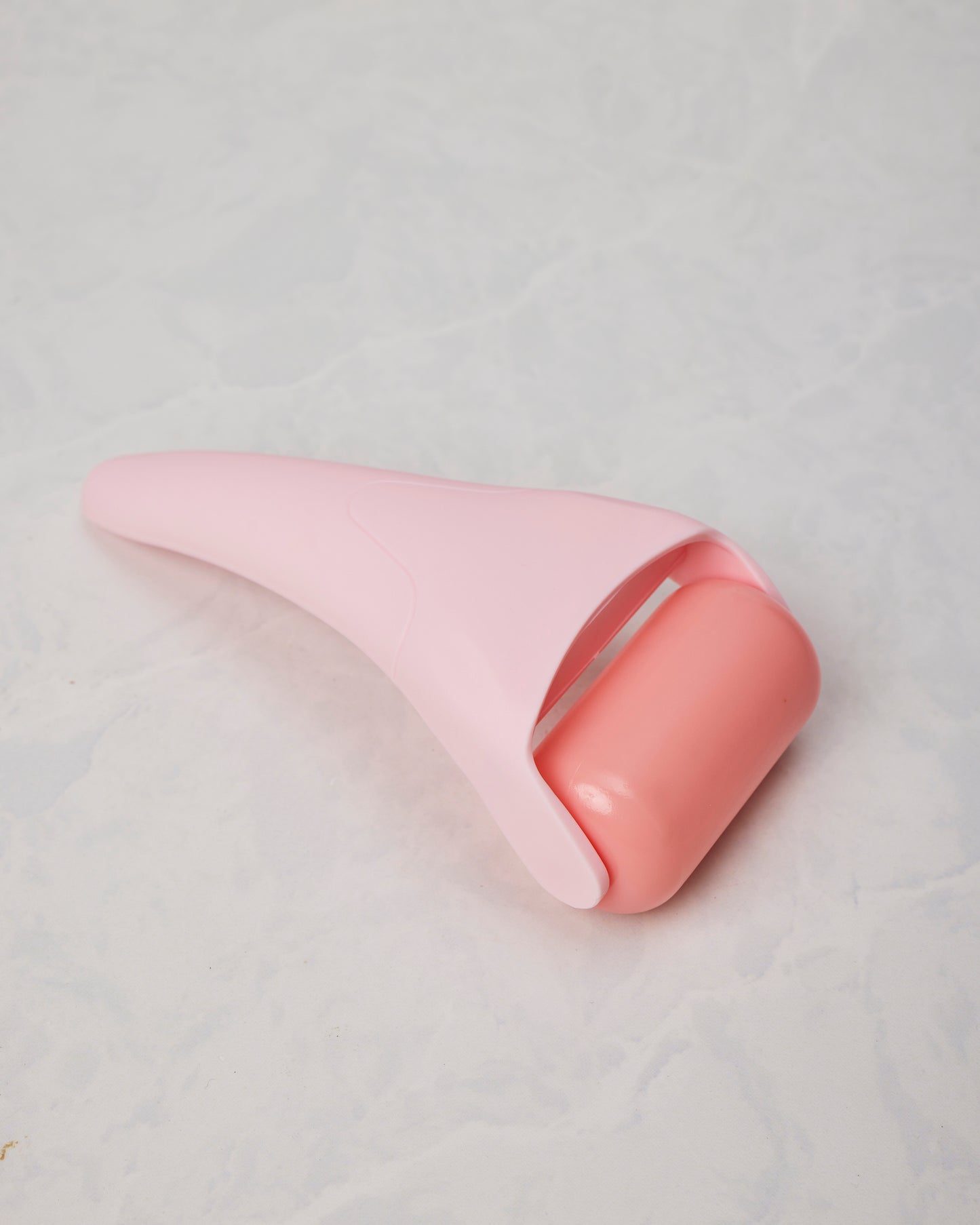 Pink ice roller shown from the roller-head side, with a rounded coral-colored roller and tapered handle.