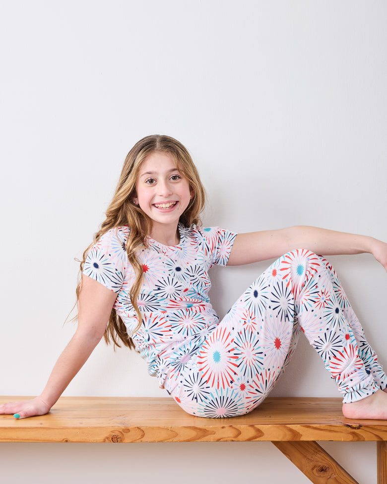 Child model seated on a bench in the fireworks-print short-sleeve pajama set