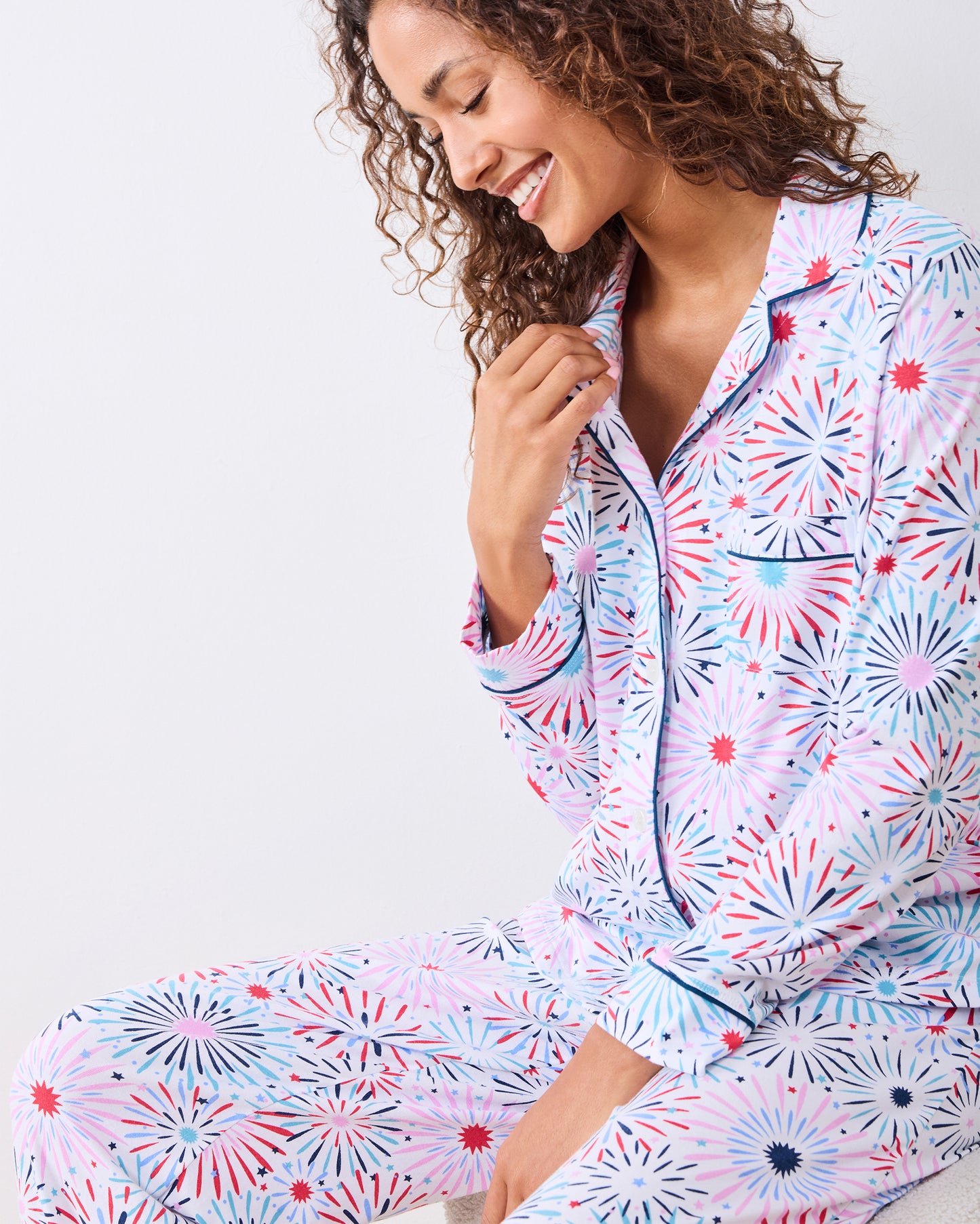 Seated studio view of the fireworks-print long pajama set with navy piping