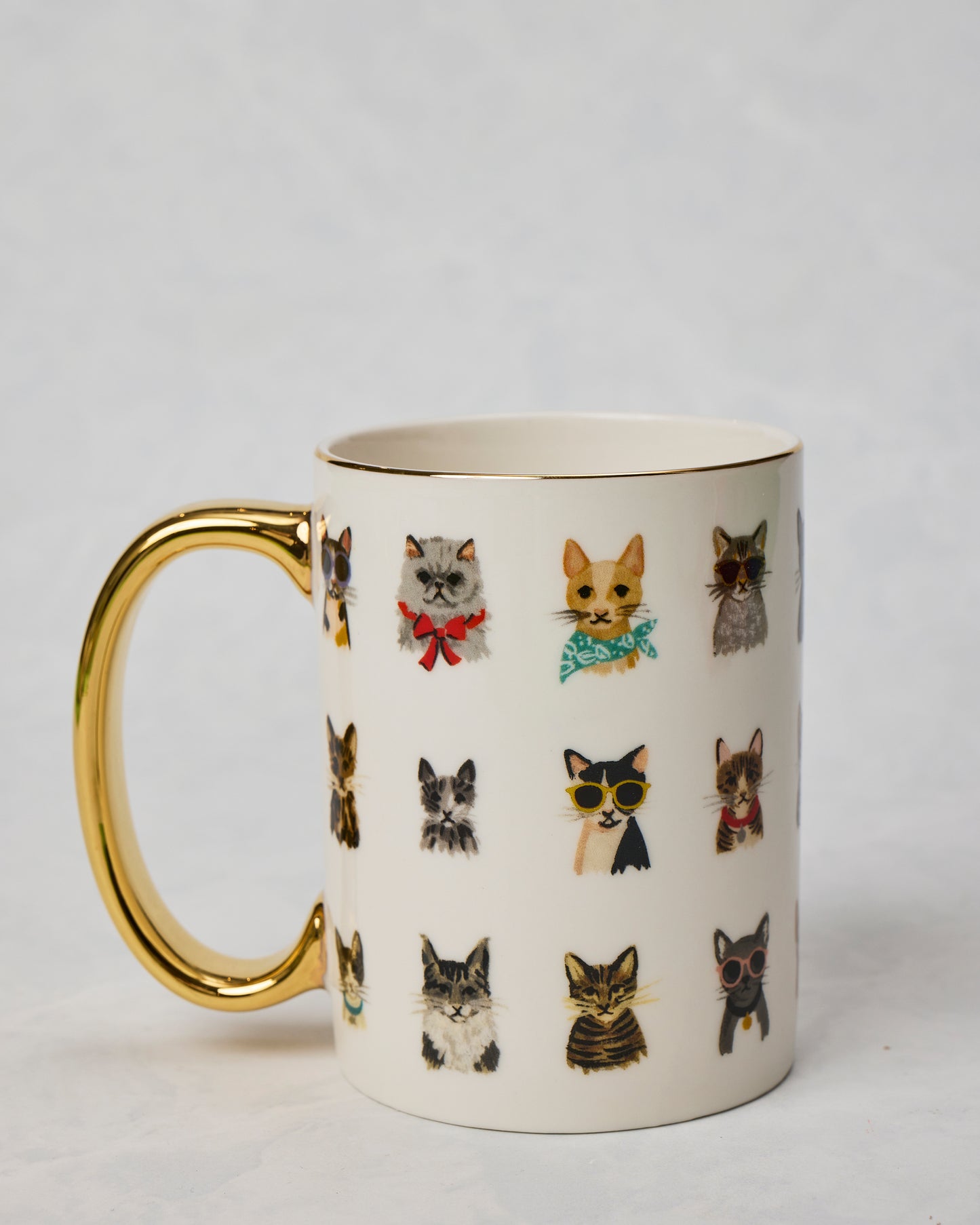 Porcelain Cool Cats mug shown from the side with a gold handle, gold rim, and rows of illustrated cats wearing accessories.