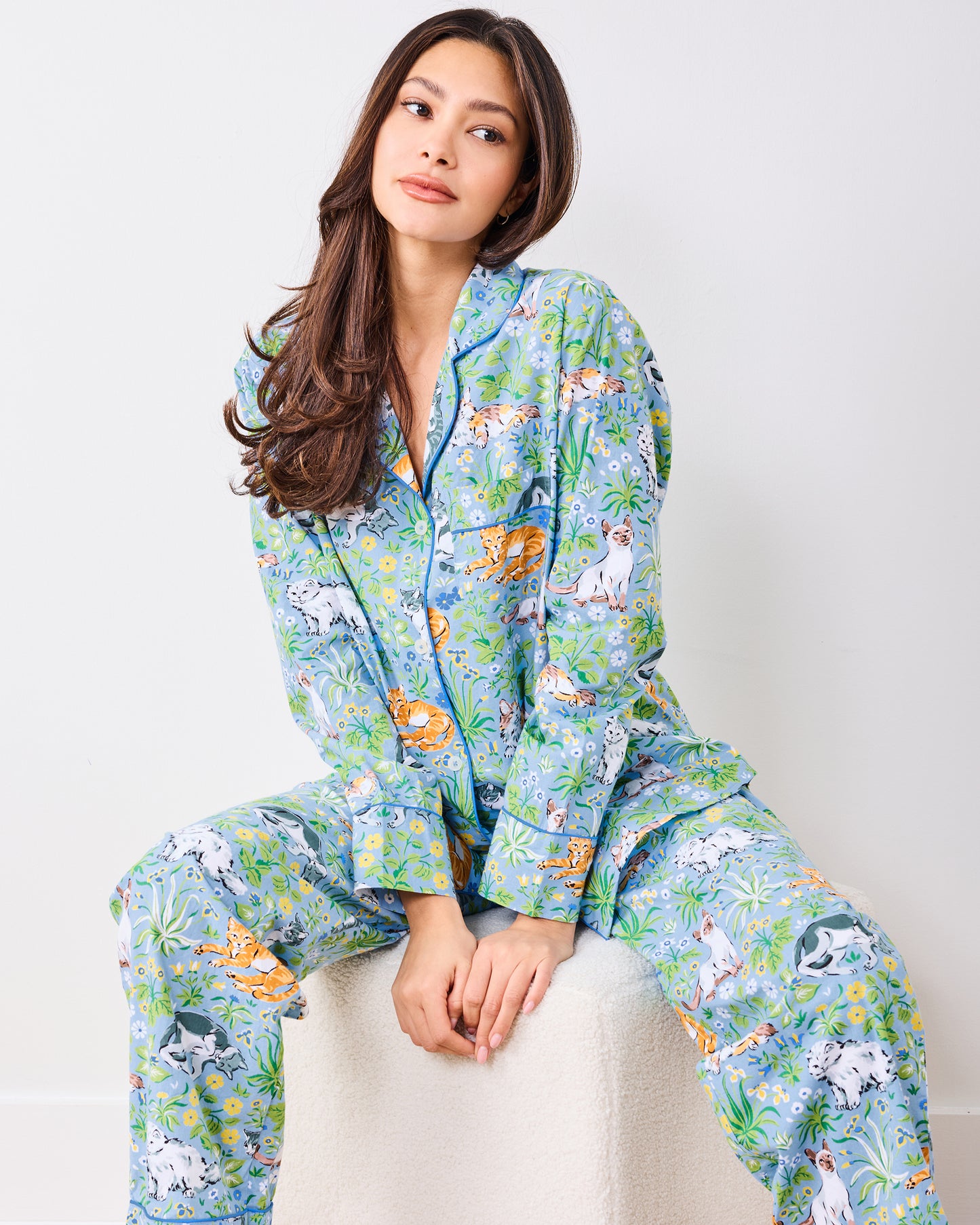 Seated full view of the blue long pajama set with cats, flowers, and greenery