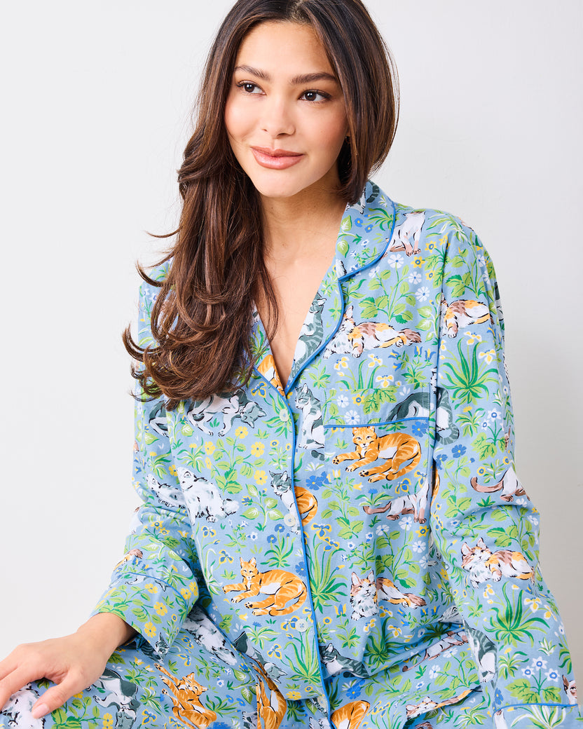 Seated close front view of the blue button-front pajama set showing the cat and garden print