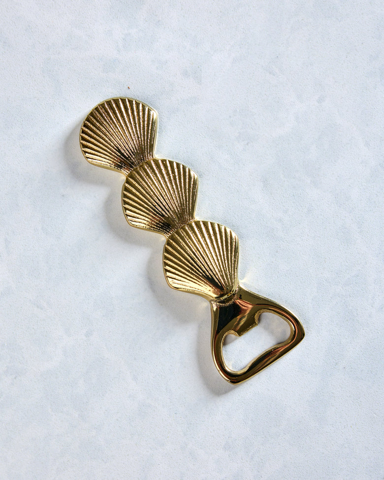 Brass bottle opener with three ridged seashell shapes arranged along the handle