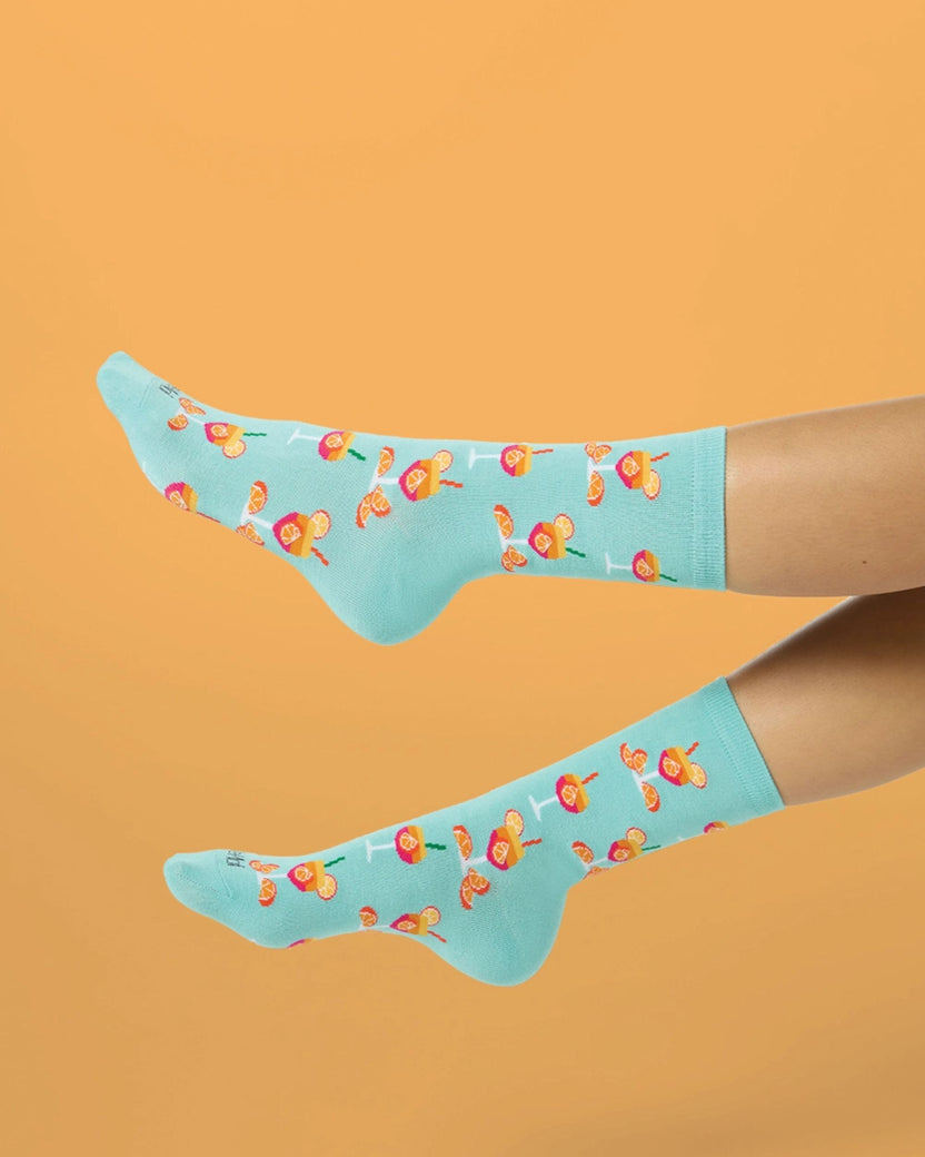 Two people wearing light blue cocktail-patterned crew socks, shown with their legs extended against an orange background.