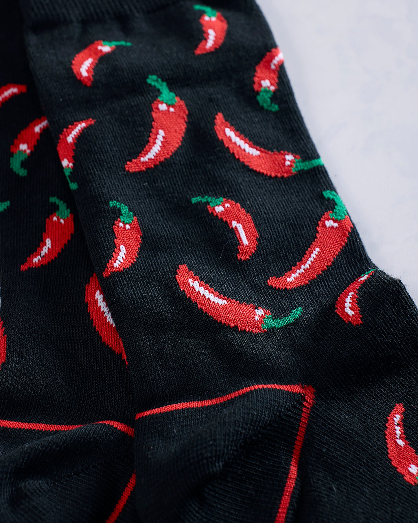 Close-up of black socks with a repeating red chili pepper pattern and red seam details.