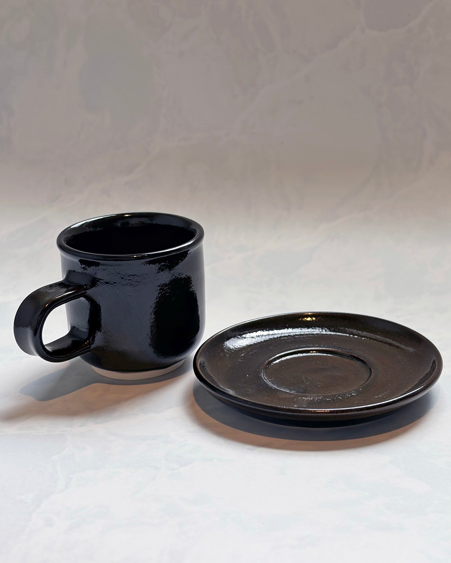Black espresso cup and matching saucer displayed separately from the front