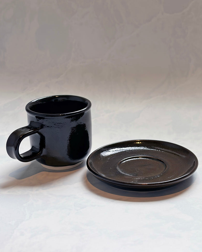 Black espresso cup and matching saucer displayed separately from the front
