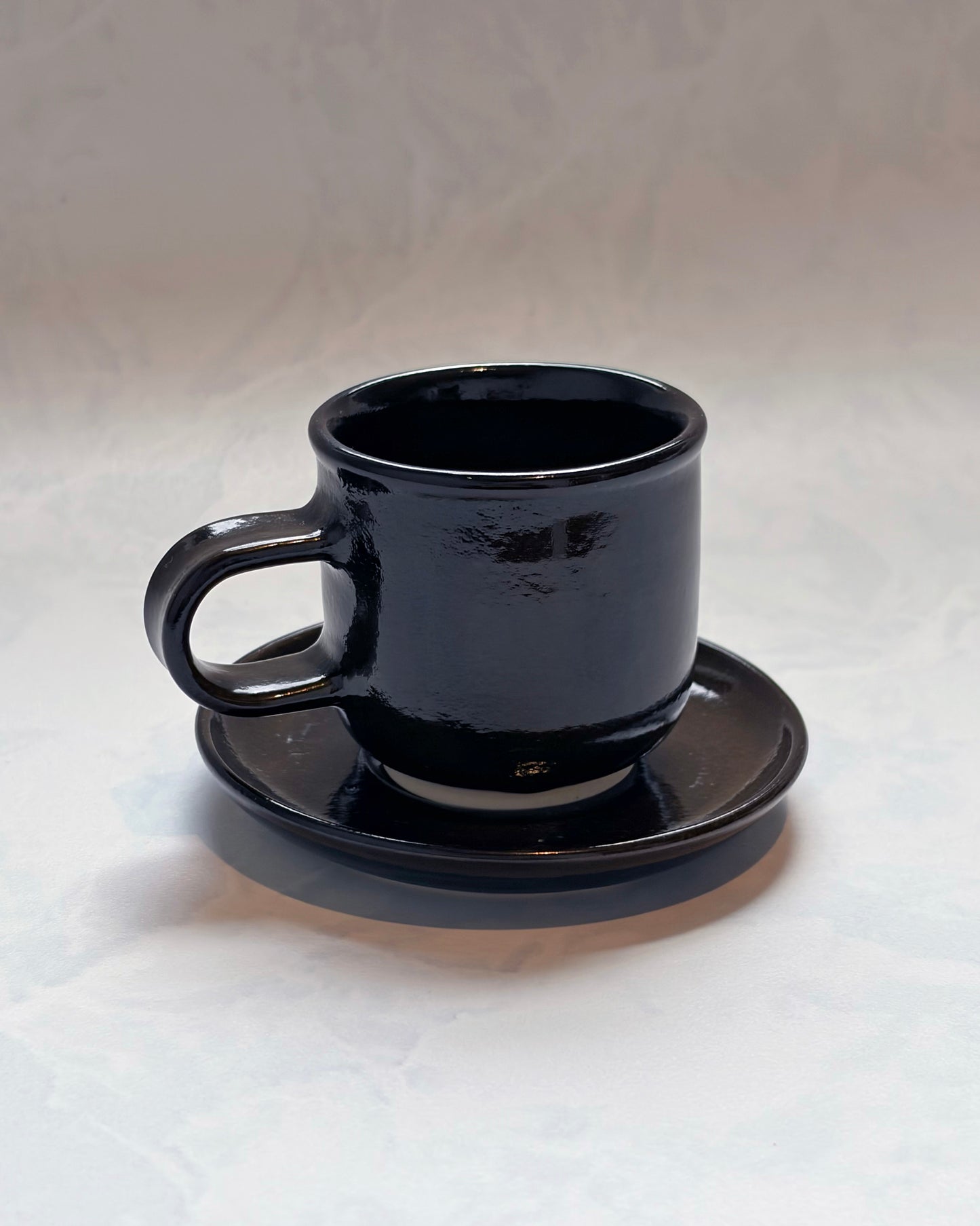 Black espresso cup resting on its matching saucer, shown from the front
