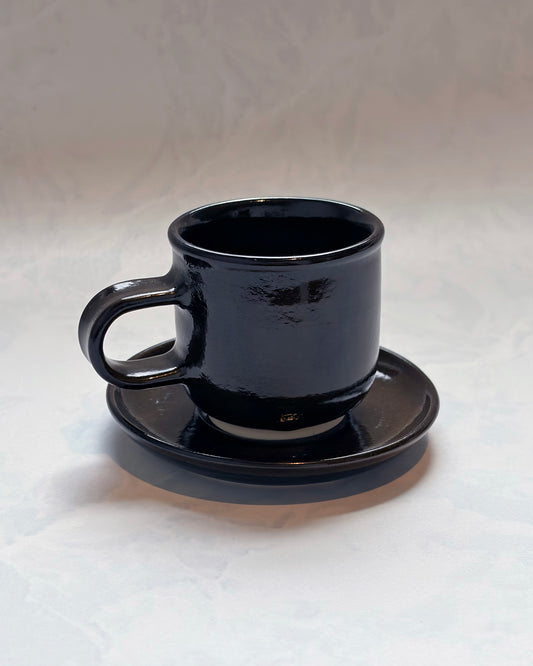 Black espresso cup resting on its matching saucer, shown from the front