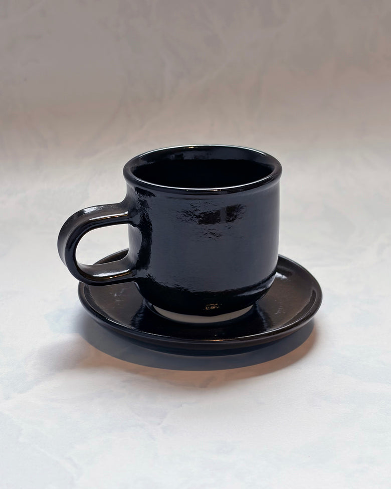 Black espresso cup resting on its matching saucer, shown from the front