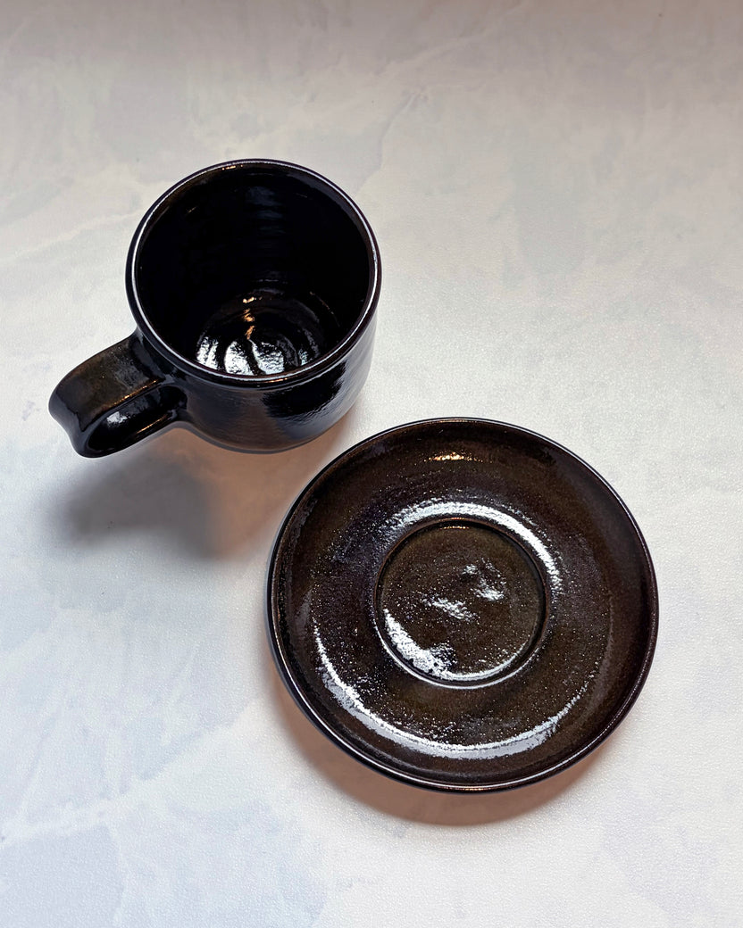 Overhead view of a black espresso cup beside its matching saucer