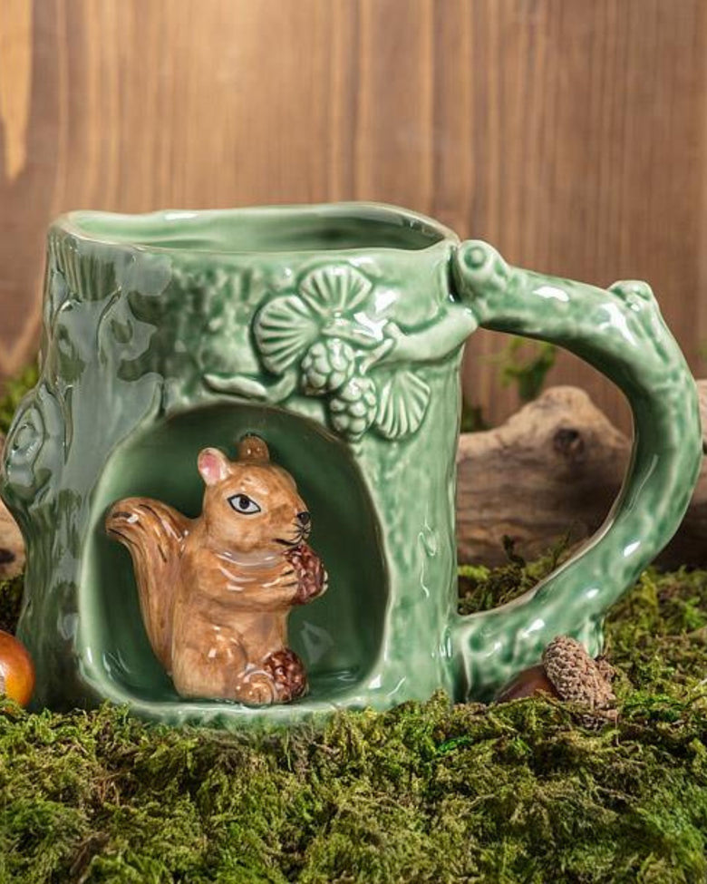 Green squirrel mug displayed on moss in a woodland-themed setting, with the squirrel figure visible in the front alcove.