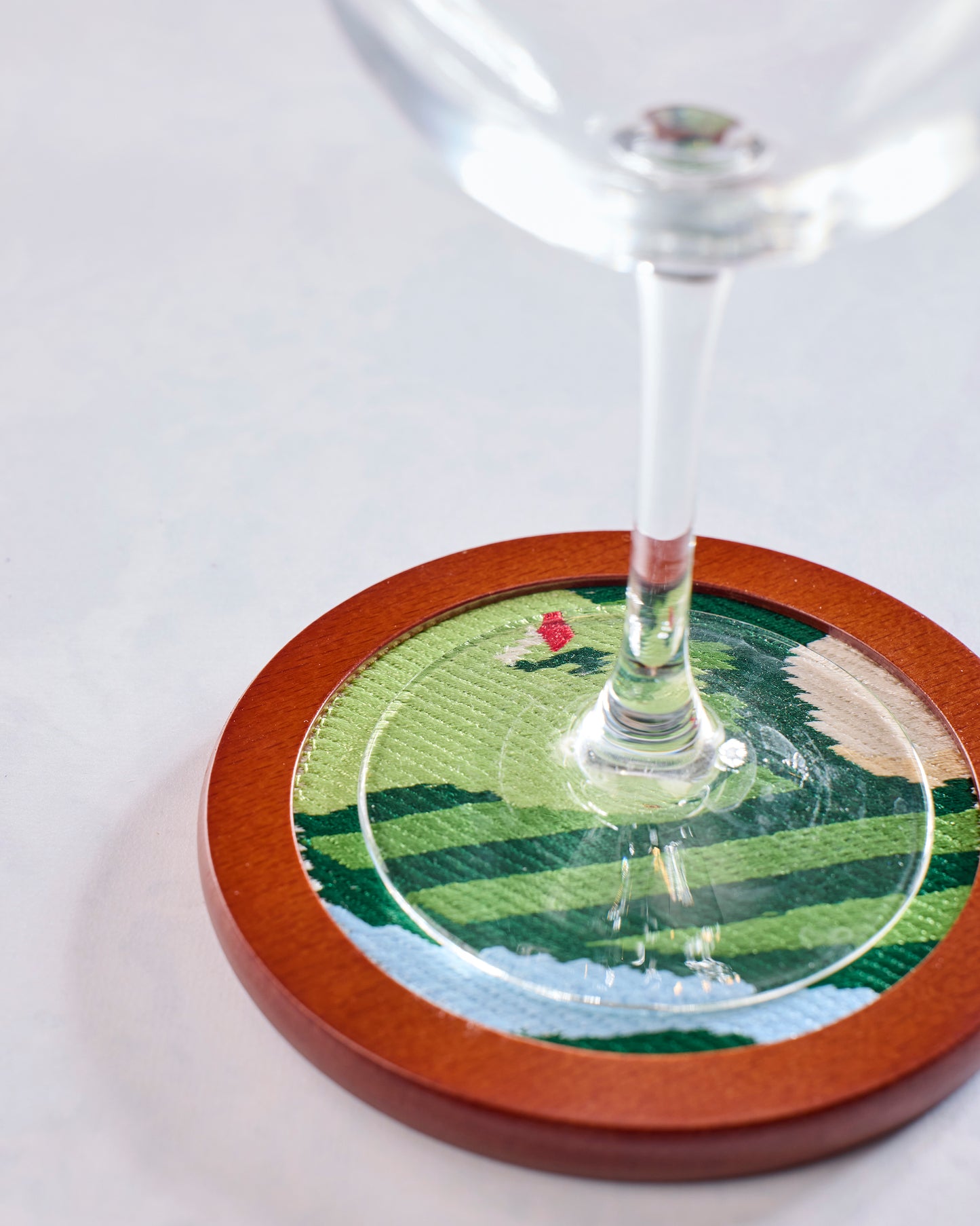 Stemmed glass resting on a round green stitched golf coaster with a red flag design.