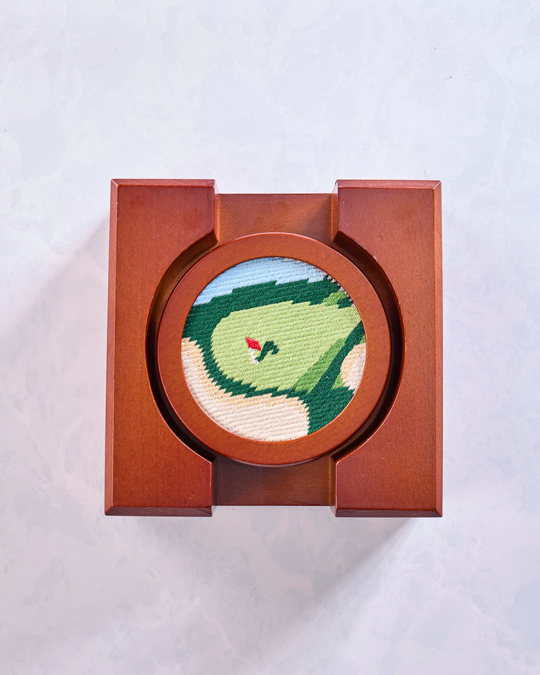 Round green stitched golf coaster with a red flag design, shown in a square wooden display frame.