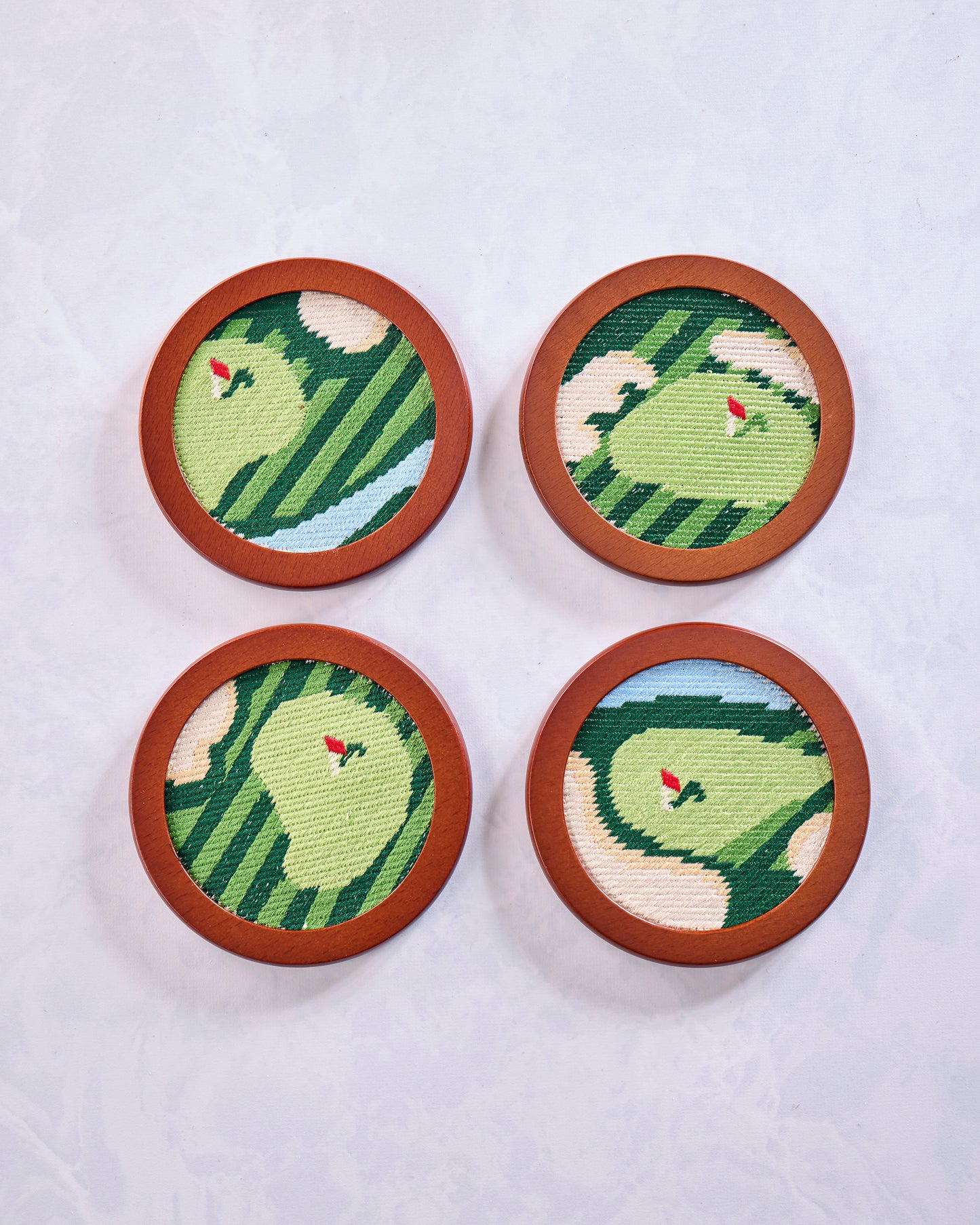 Four round green stitched golf coasters arranged in a two-by-two layout, each with a red flag design.