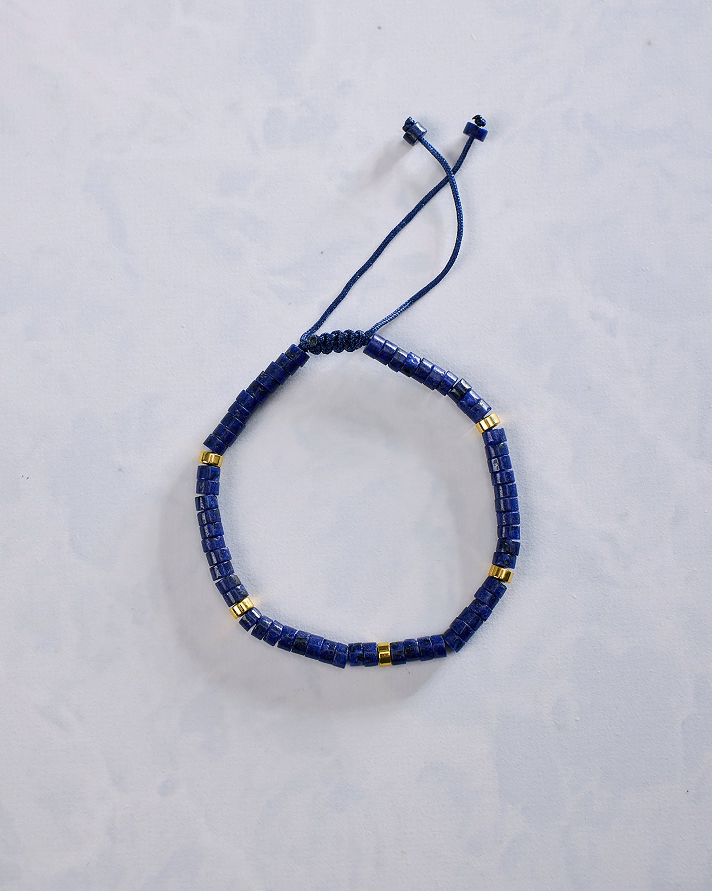 Blue beaded bracelet arranged in an oval, with small gold-tone accent beads and an adjustable cord closure.