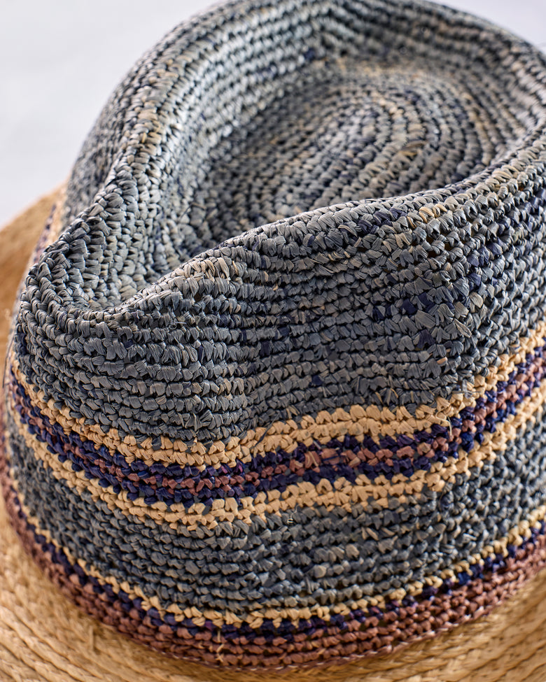 Close-up of the crocheted fedora showing its blue-gray crown and contrasting tan and dark stripes.