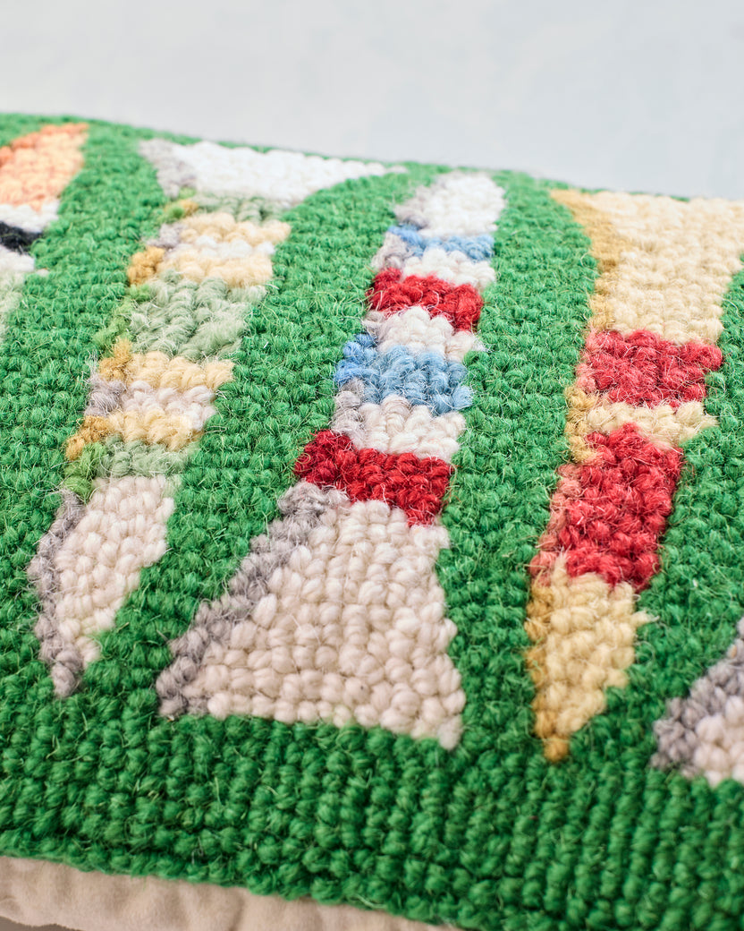 Close-up of the golf-tees pillow’s multicolored hooked design on a green background.