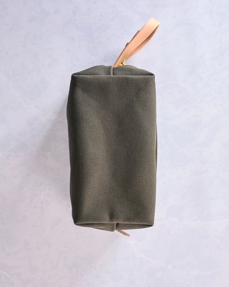 Side view of the olive canvas travel kit showing its rectangular profile and leather wrist strap.