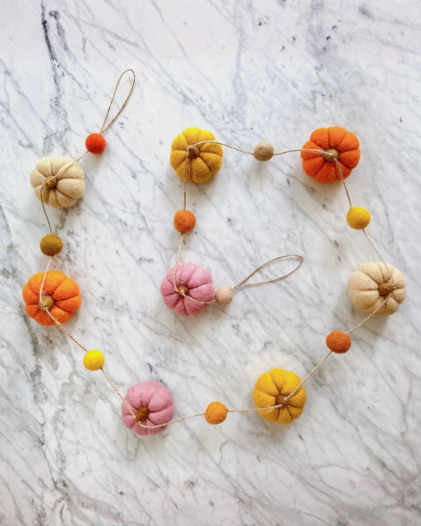 Pumpkin garland arranged in a loose circle, with orange, yellow, pink, and cream pumpkins connected by string.