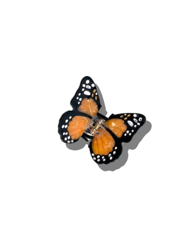 Hand-painted orange-and-black butterfly claw hair clip shown from above, with white spot details and a clear center hinge.