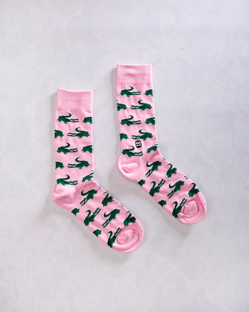 Pair of pink crew socks with a repeating dark green alligator pattern.