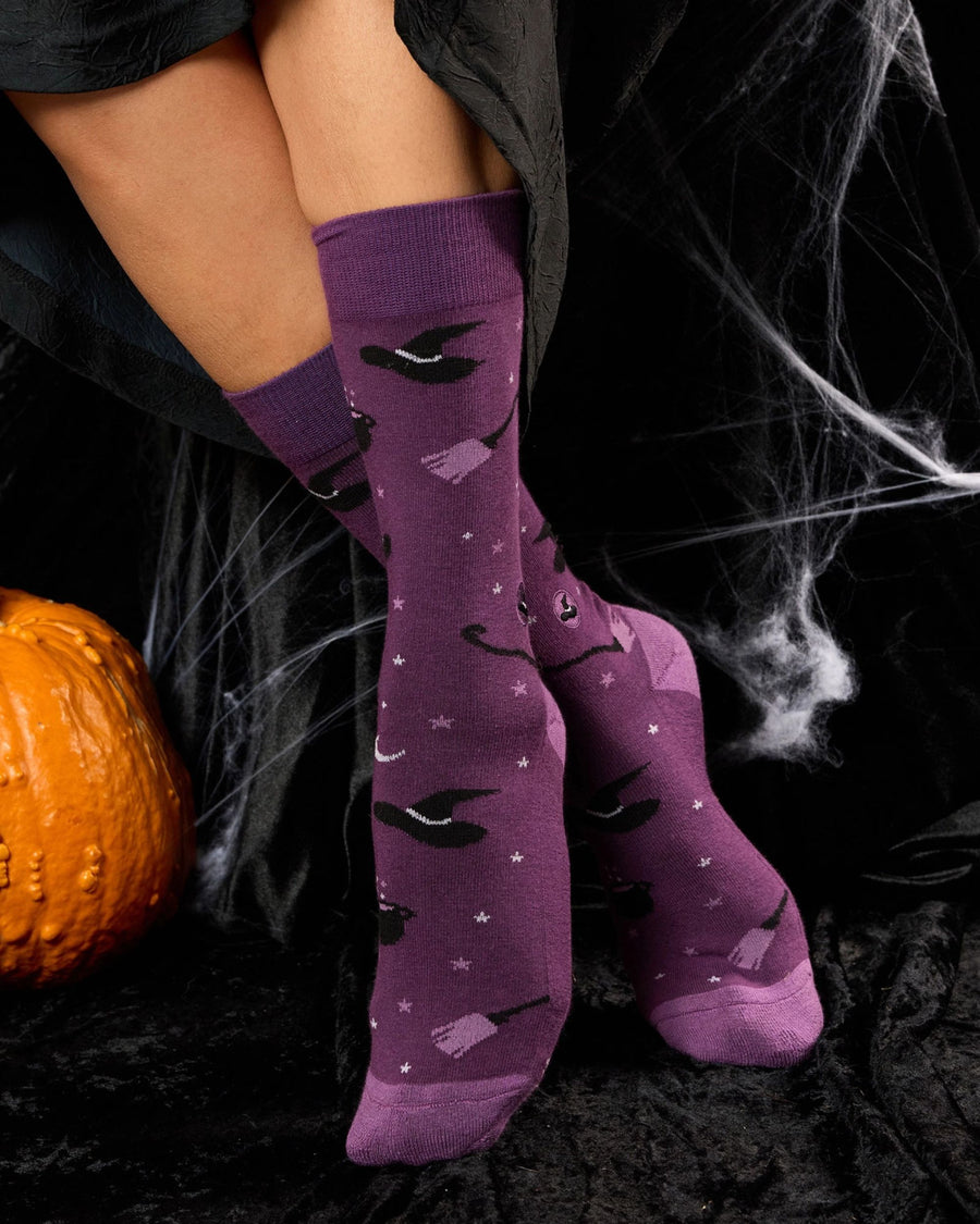 Purple patterned socks worn on lower legs, showing witch hats, cauldrons, broomsticks, stars, and moons.