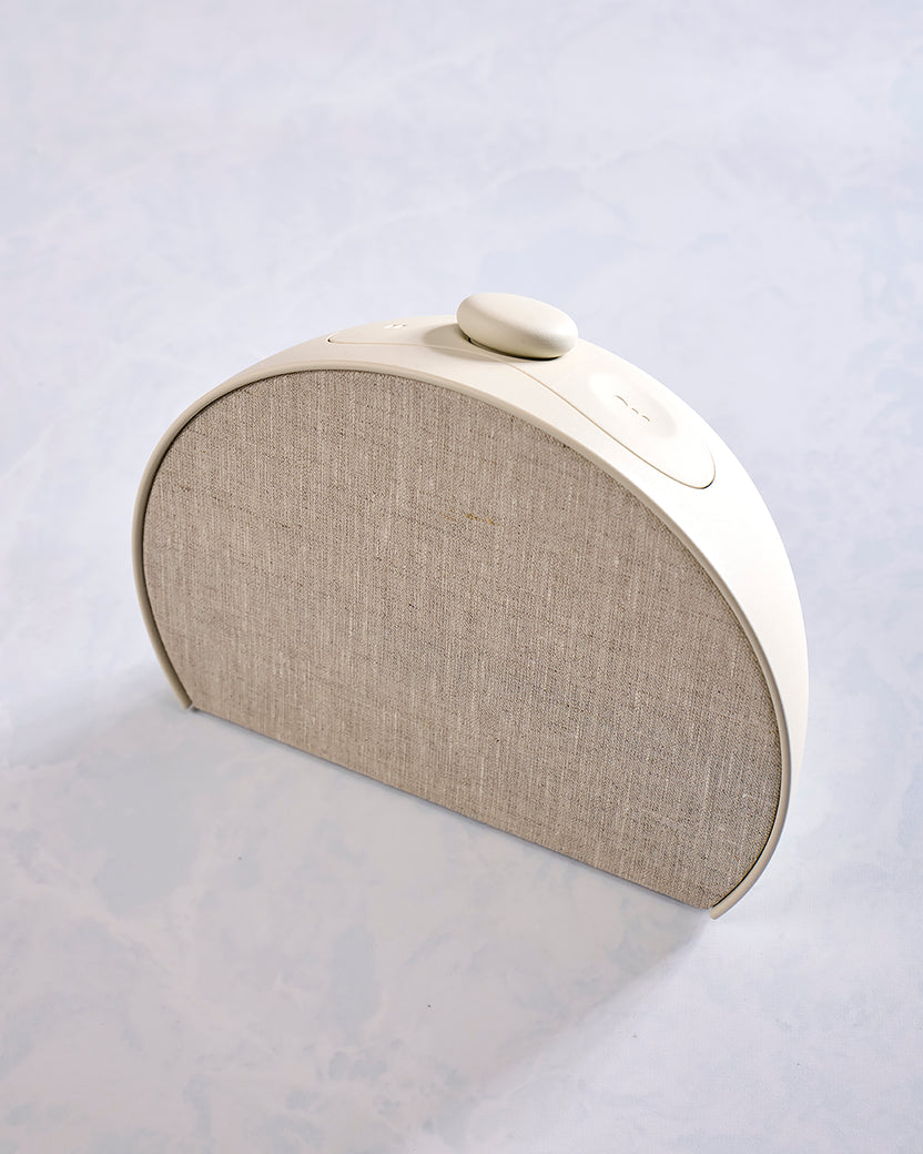 Angled front view of the putty-colored Restore 3 sunrise alarm clock, showing its fabric grille and top controls.