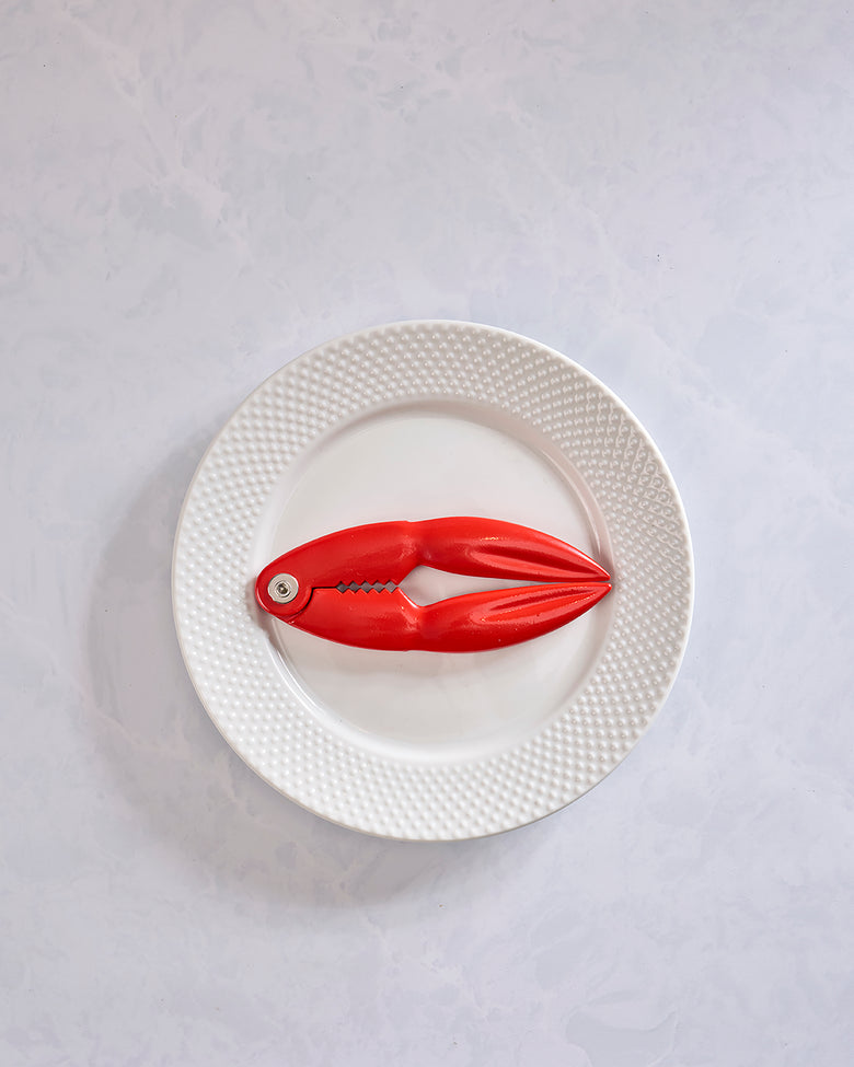 Red lobster-shaped shell cracker displayed open on a white textured plate.