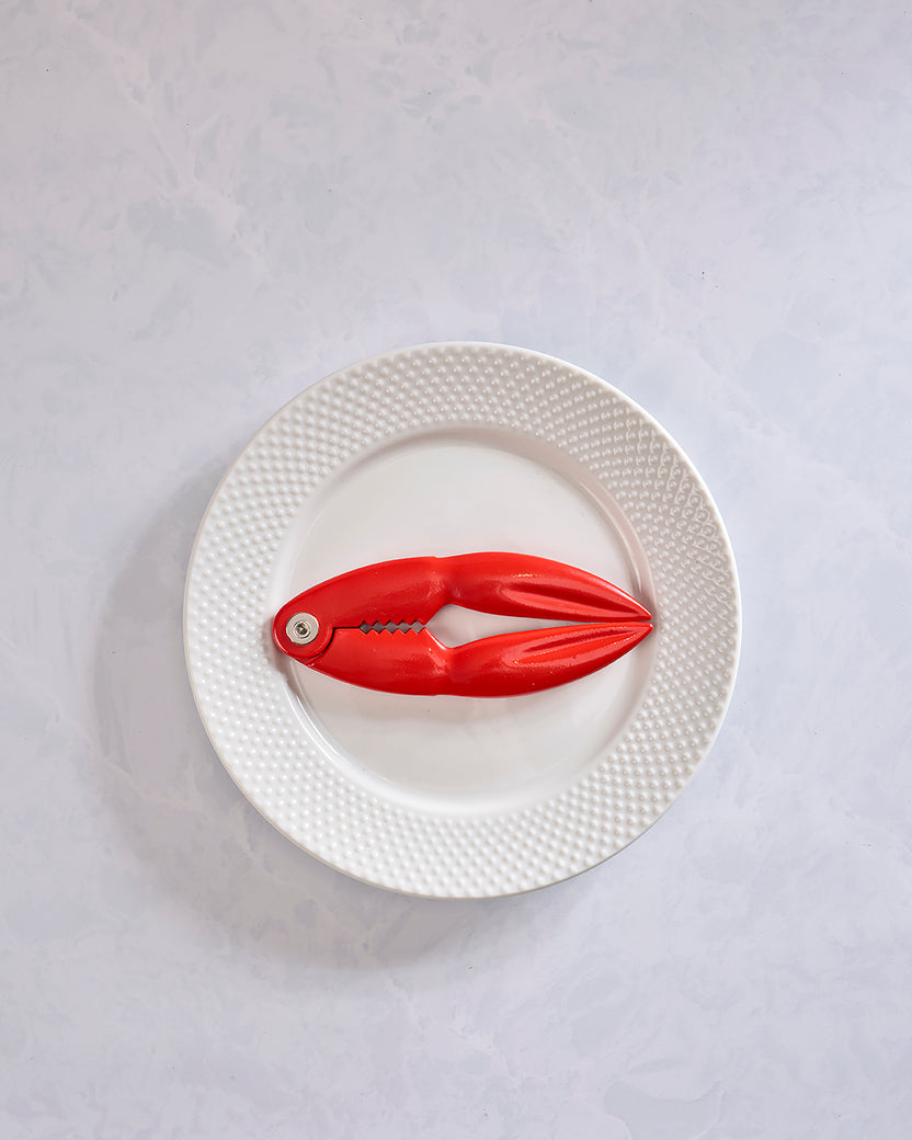 Red lobster-shaped shell cracker displayed open on a white textured plate.