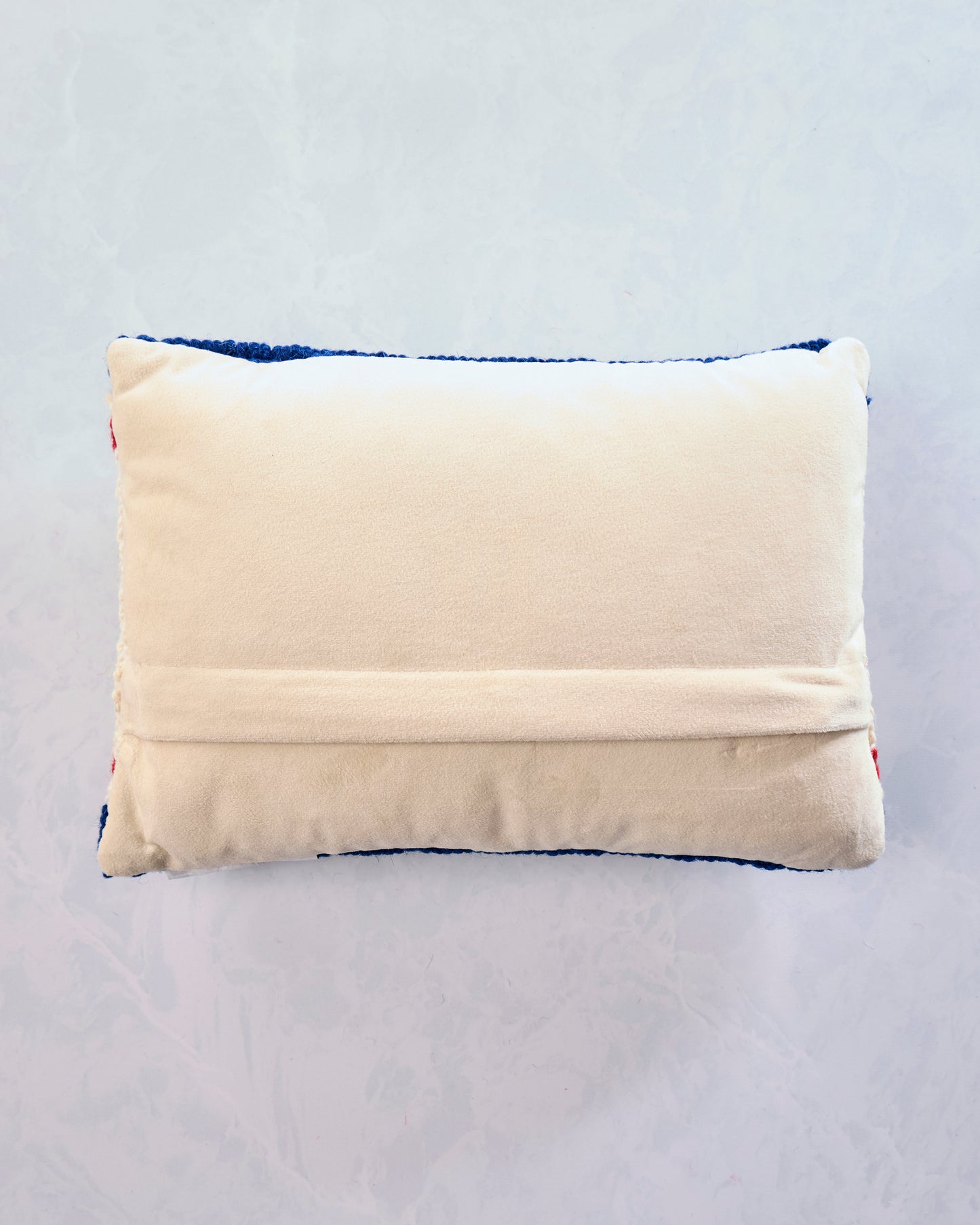 Back view of the red, white, and blue Americana Stars USA lumbar pillow, showing its cream velvet backing and zipper flap.