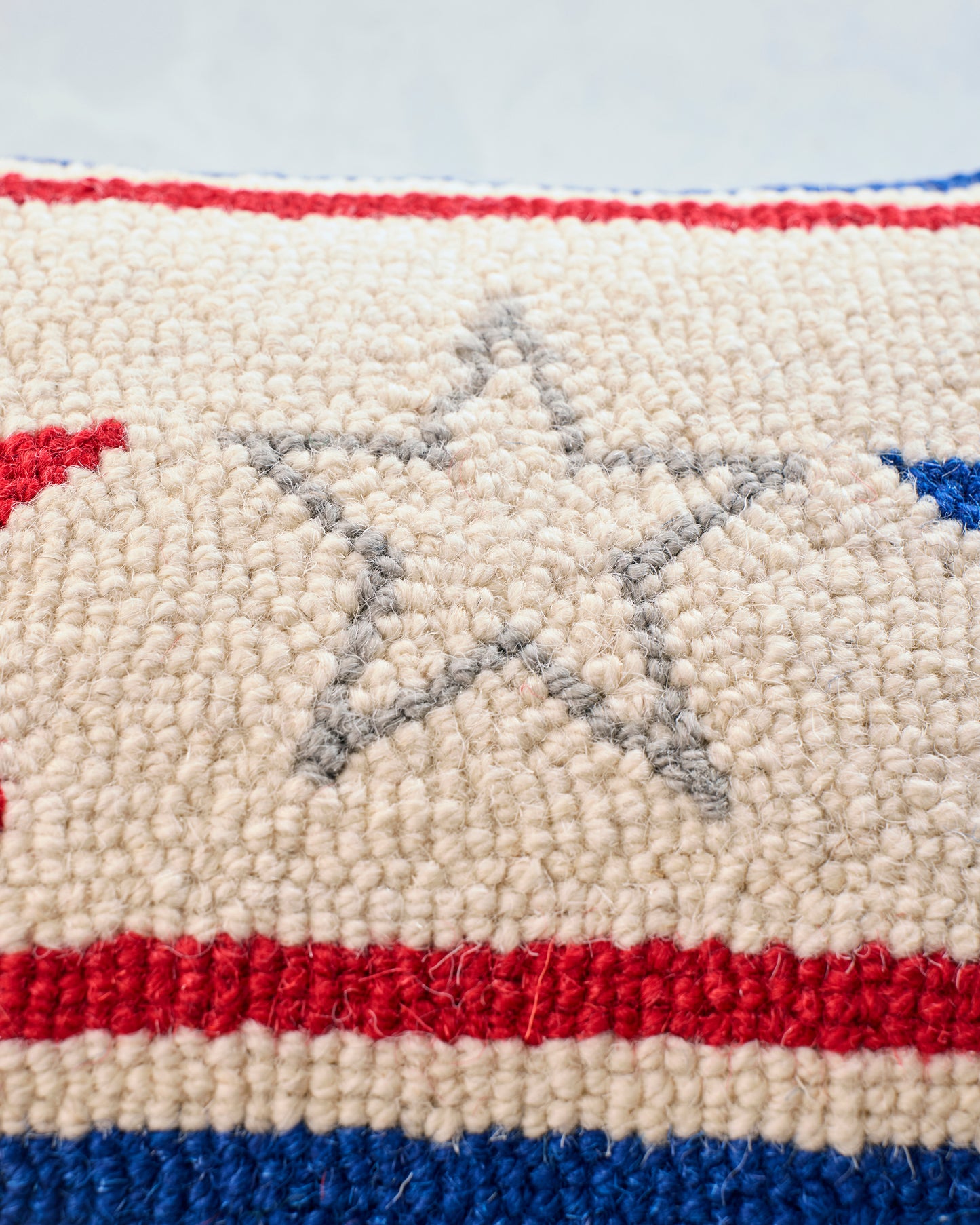 Close-up of the Americana pillow’s hooked front, showing cream fabric, red and blue stripes, and a gray outlined star.