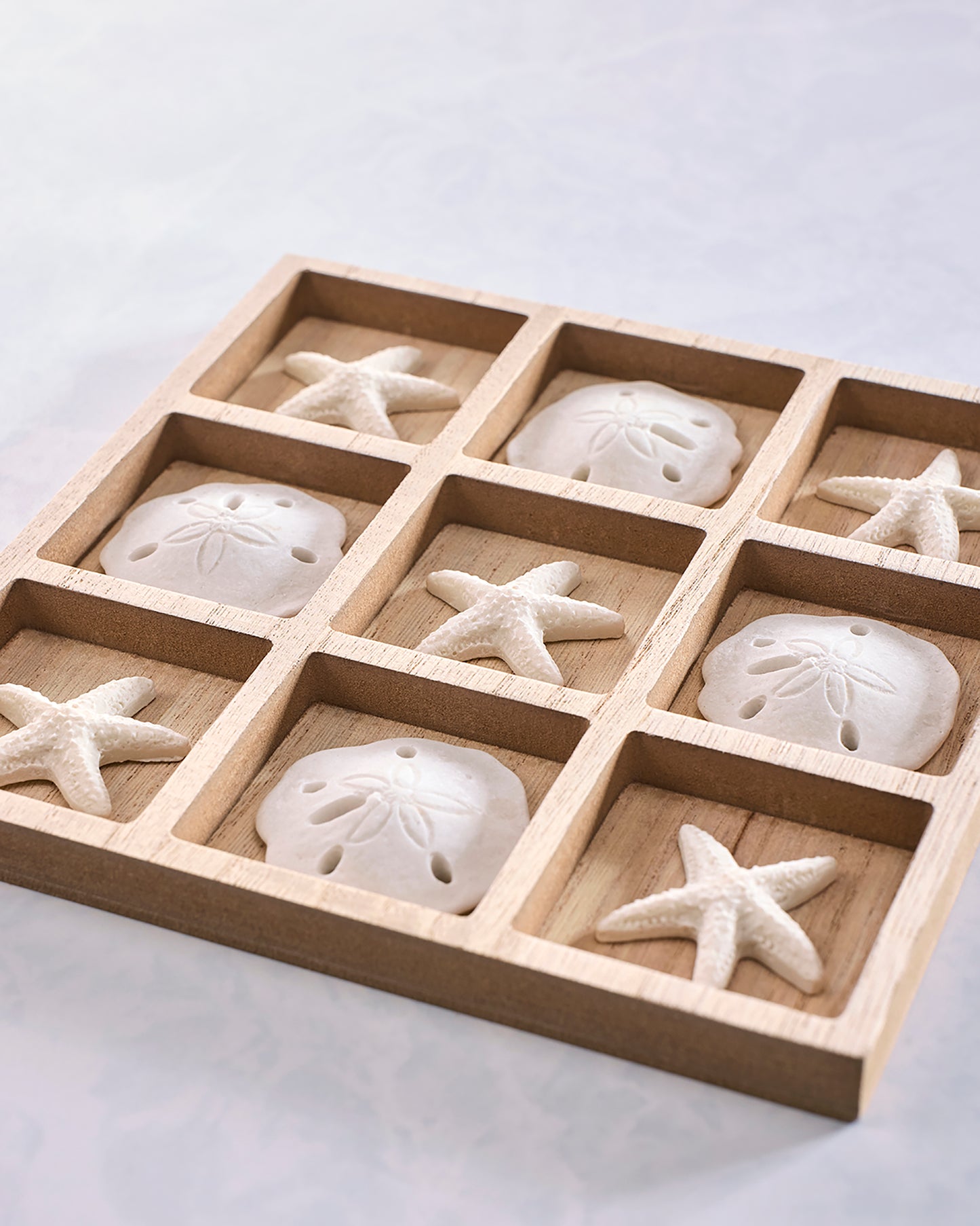 Angled close view of a wooden tic-tac-toe board holding starfish and sand-dollar-shaped playing pieces.
