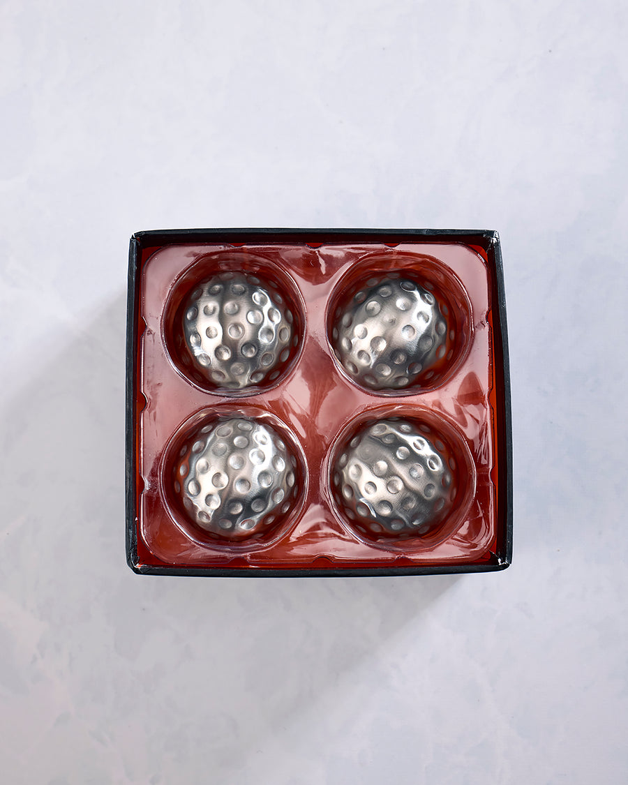 Open package containing four silver dimpled metal chilling cubes in a red tray.
