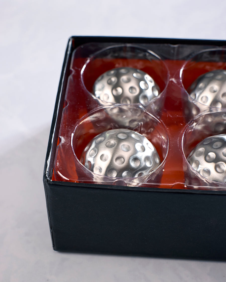 Close-up of four silver dimpled chilling cubes in the open black package tray.