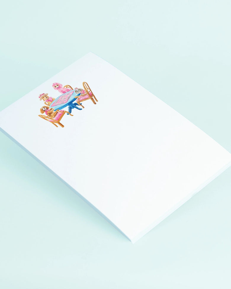 Angled view of a white notepad with a dogs-playing-mahjong illustration near the top.