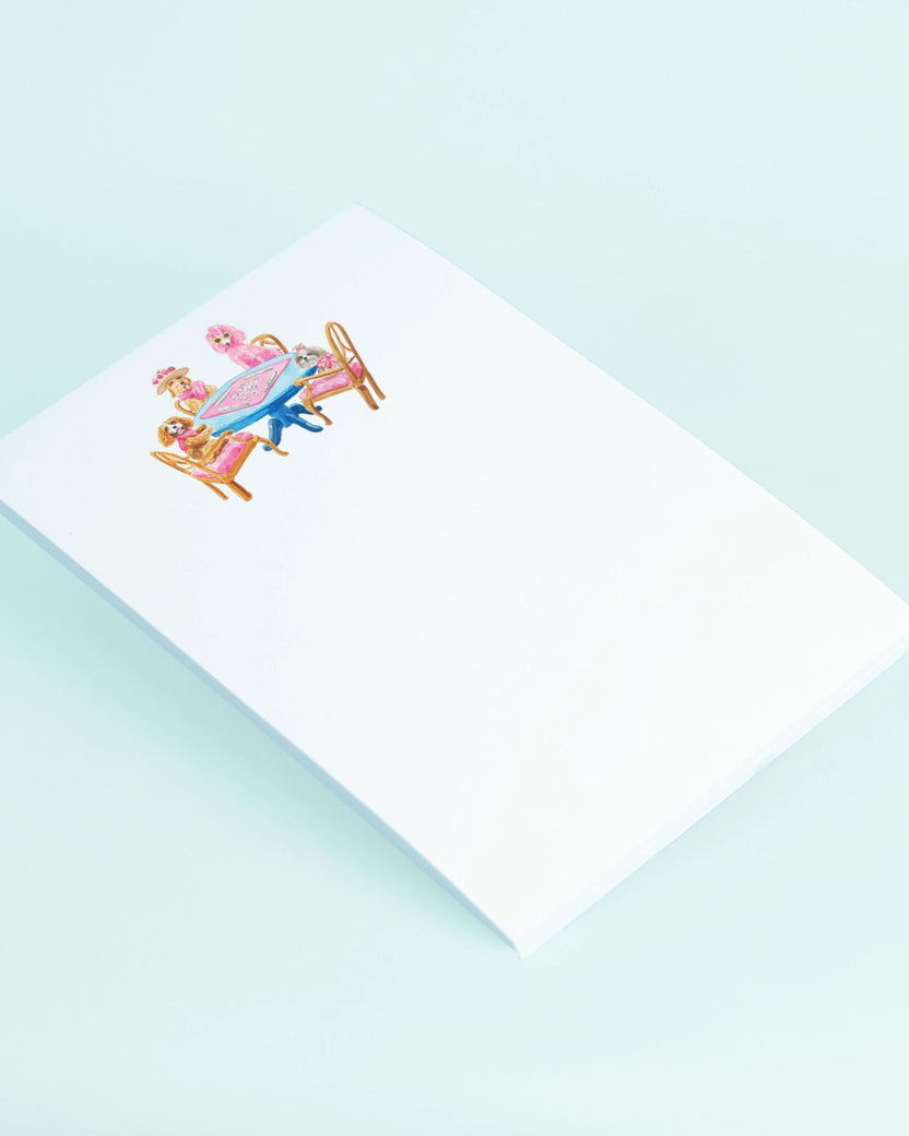 Angled view of a white notepad with a dogs-playing-mahjong illustration near the top.