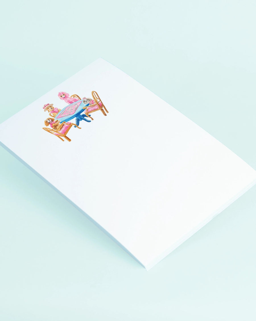 Angled view of a white notepad with a dogs-playing-mahjong illustration near the top.